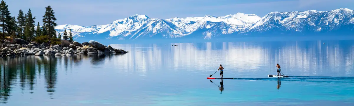 Paddleboarders on Lake Tahoe with snow-capped mountains in the background