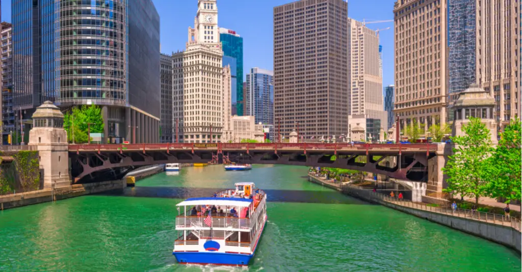 View of a boat on the Chicago River with a bridge and skyscrapers in the background.