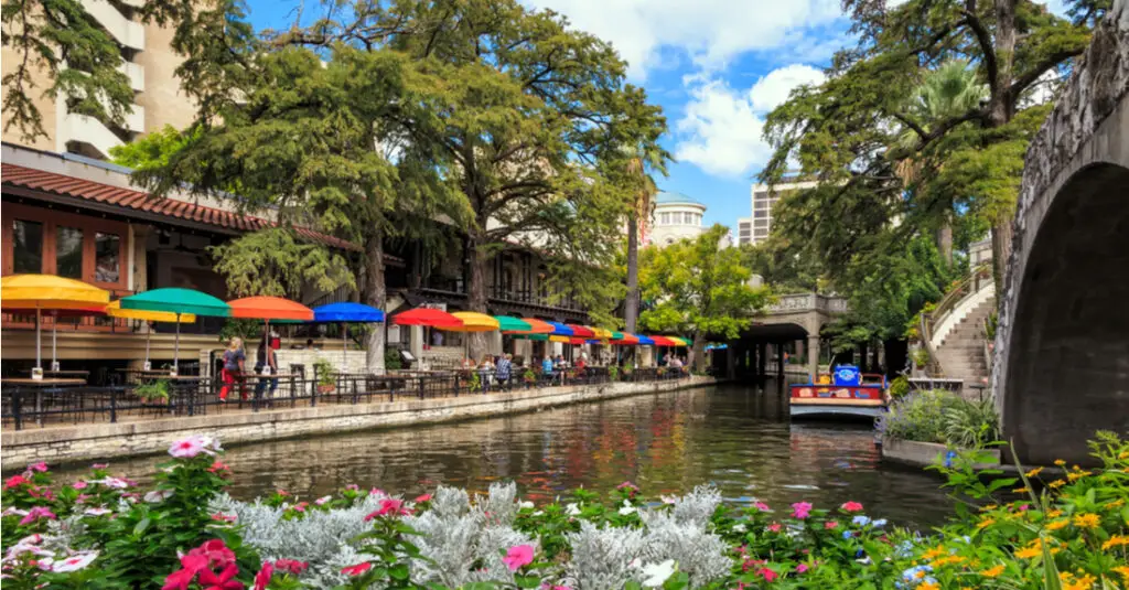 View along the San Antonio River Walk, with colorful umbrellas, a bridge and a boat.