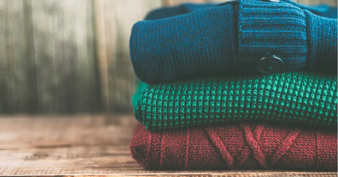 A stack of three folded sweaters (blue, green and red in color) waiting to be packed for a ski trip.